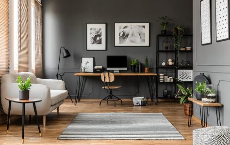 Posters on grey wall above wooden desk with computer monitor in modern workspace interior with plants